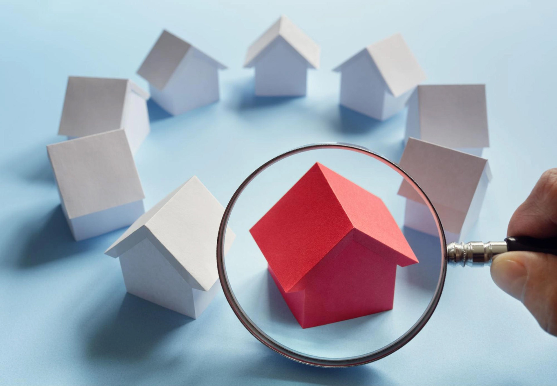 A handful of block houses with a magnifying glass over a red house.