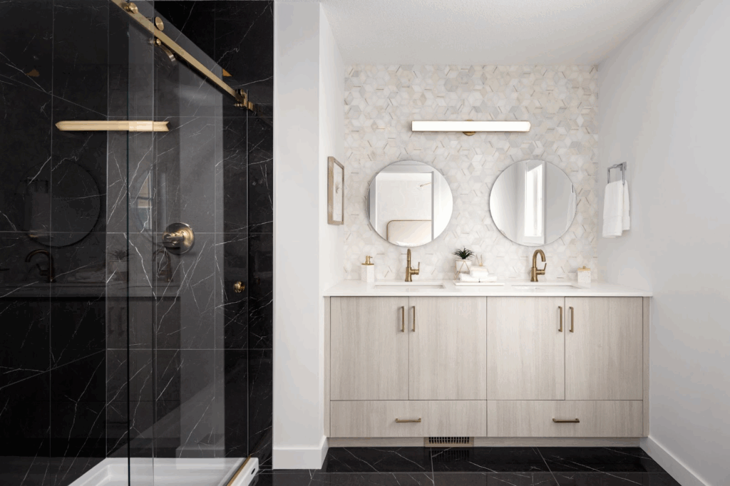 Modern bathroom with a double vanity, round mirrors, brass fixtures, and a black tile walk-in shower with glass doors in a new construction home.