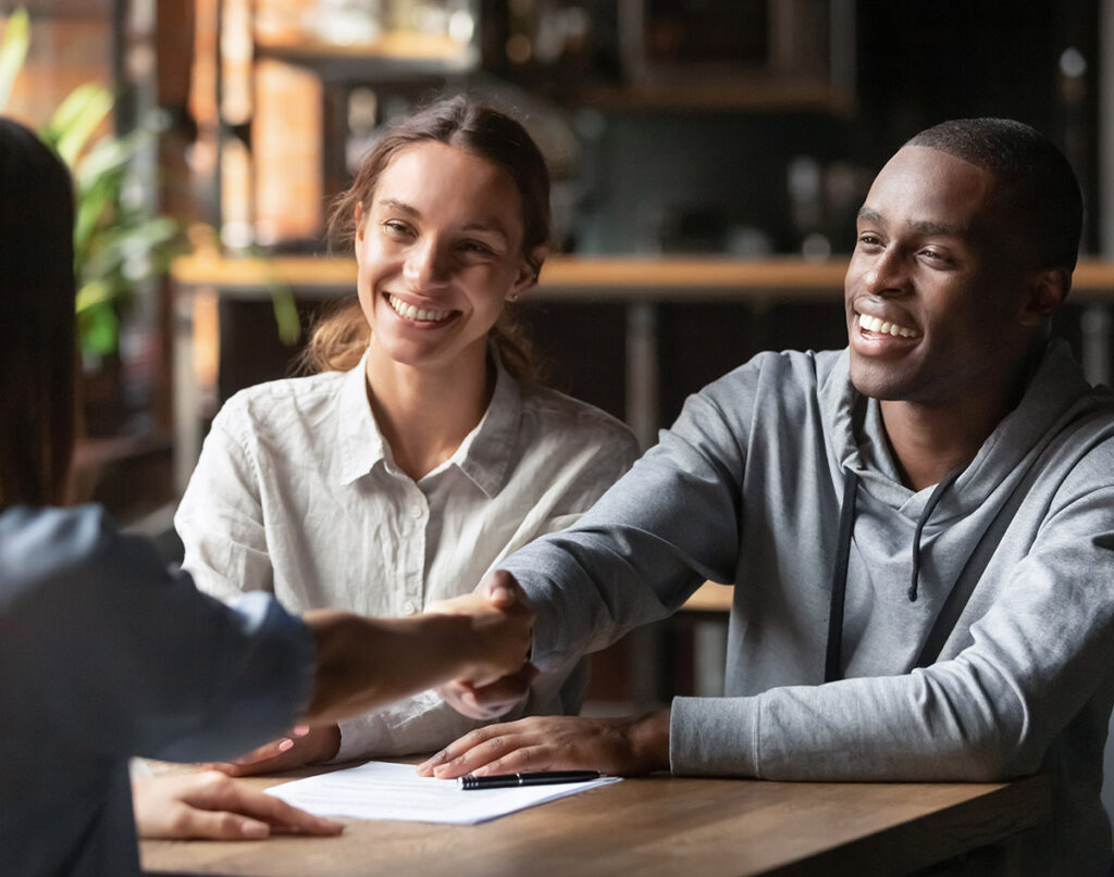 A couple shaking hands with a Shane Homes community manager at a table, engaged in a conversation about their new construction home.