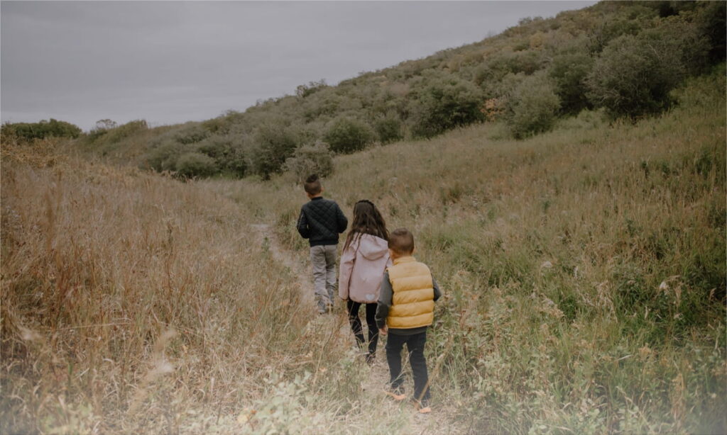 A family of four walking together in a lush green field, enjoying a sunny day outdoors.