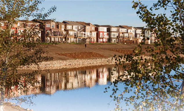 A row of colorful houses lining the serene shore of a tranquil lake under a clear blue sky.