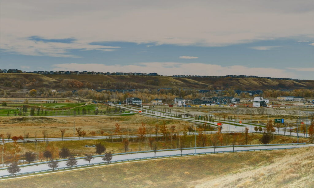 A scenic view of a winding road alongside a hillside dotted with houses under a clear blue sky.