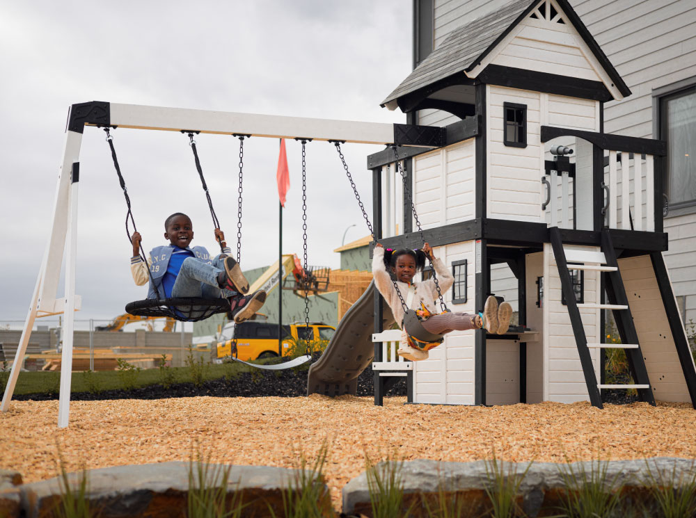 Two children joyfully playing on a swing set in a sunny outdoor playground.